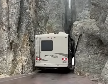 An RV stuck between narrow rocks with awning damage